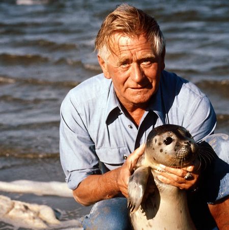 Heinz Sielmann am Strand hält ein Robbenjunges hoch