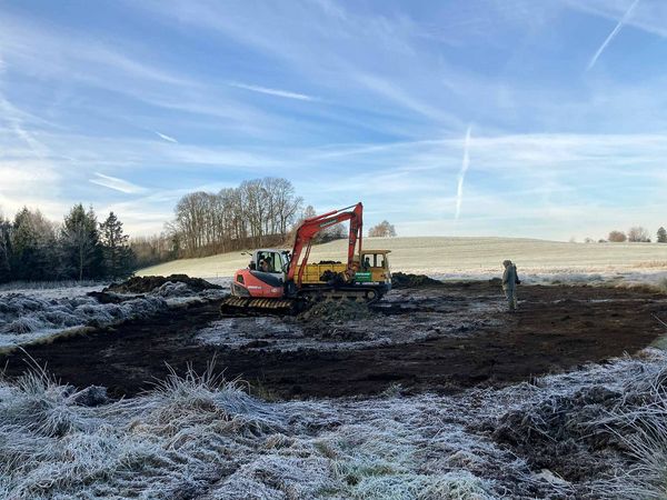 Ein Bagger hebt einen Tümpel auf einem gefrorenen Acker aus.