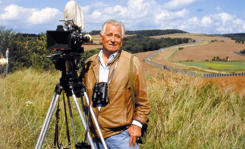 Heinz Sielmann steht hinter seiner Kamera vor einer sommerlichen Landschaft