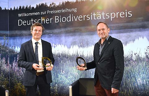 Zwei Herren halten ihren Preis in den Händen auf einer Bühne