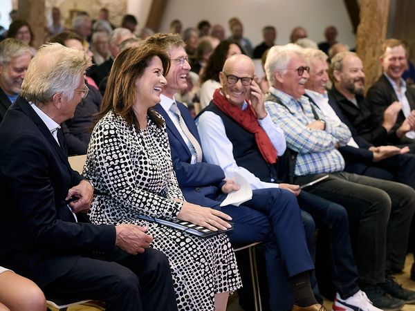 Mehrere Herren und eine Dame sitzen in der ersten Reihe bei einer Veranstaltung