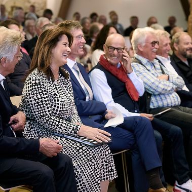 Mehrere Herren und eine Dame sitzen in der ersten Reihe bei einer Veranstaltung