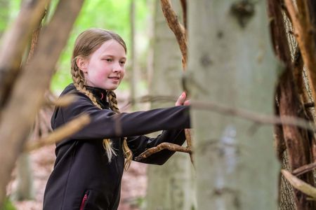 Mädchen baut ein Tippi im Wald aus Ästen
