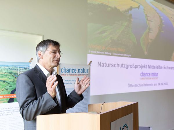 Leiter des Biosphärenreservats Mittelelbe Guido Puhlmann am Rednerpult. Rechts ist die Projektion einer PowerPoint-Folie mit Elbefoto.