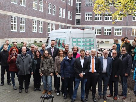Gruppenfoto vieler Personen vor einem weißen Auto