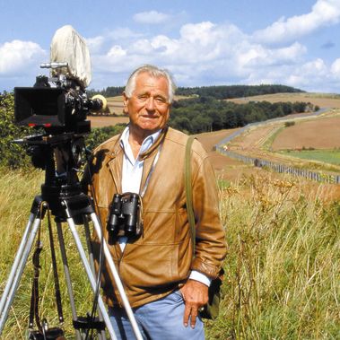 Heinz Sielmann mit Kamera und Fernglas vor einer Landschaft