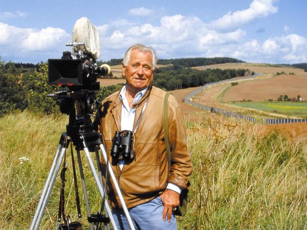 Heinz Sielmann mit Kamera und Fernglas vor einer Landschaft