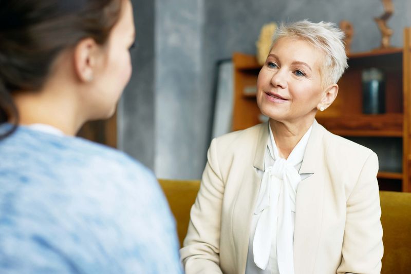 Dame in hellem Blazer sitzt einer anderen Frau gegenüber und unterhält sich mit ihr