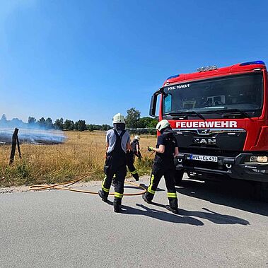Zwei Feuerwehrleute stehen vor einem roten Feuerwehrauto.