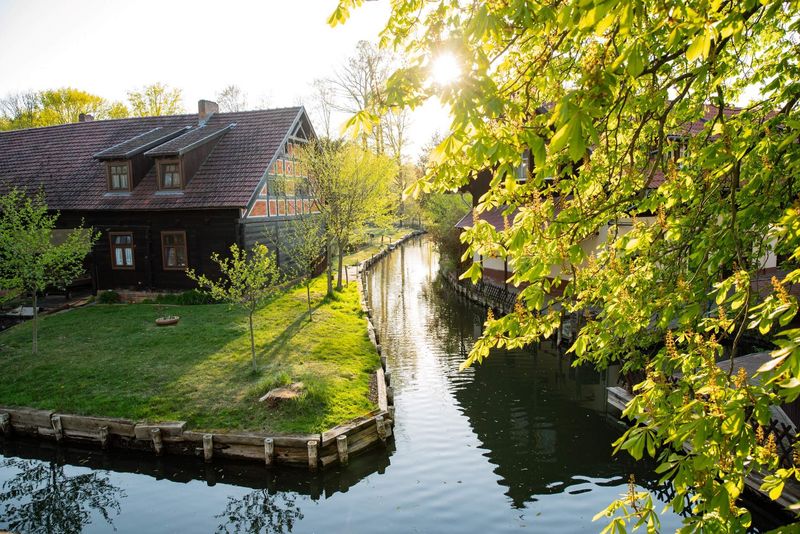 Ein Gewässer im Spreewald mit typischem kleinen Haus wird beschienen von der Sonne