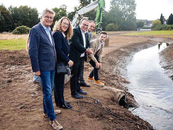 Fünf Personen stehen an einem neu angelegten Bachlauf.