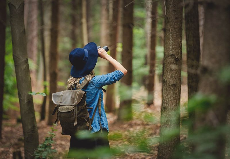 Frau schaut durch ein Fernglas und steht im Wald